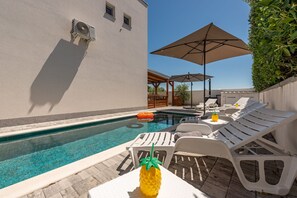 Una piscina con sillas de descanso y sombrillas, una decoración de piña y un edificio con unidad de aire acondicionado.