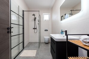 Un baño moderno con cabina de ducha de vidrio, un lavabo blanco y un estante de madera.