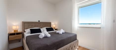 A bedroom with a bed, nightstands, a window with a view, and a wooden floor.