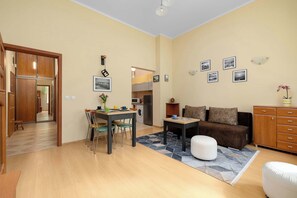 Ein Wohnzimmer mit Sofa, Hocker, Esstisch, Stühlen und einer Küche im Hintergrund.