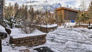A modern building with a stone facade, a metal railing, and a view of snow-covered mountains. - Spring Creek Courtyard Retreat | Hot Tub, Pool Table & Trailside Access (Canmore)