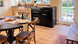Una cocina con gabinetes de madera, una mesa de comedor con sillas, un refrigerador y una ventana con vista a la vegetación.
