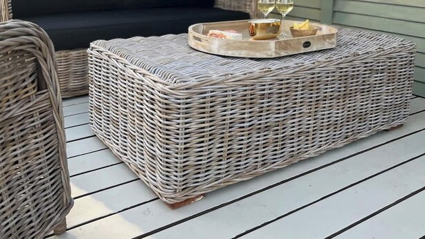 Un espacio de estar al aire libre cubierto, con mobiliario de mimbre y una mesa redonda con bebidas.