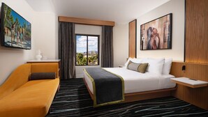 Une chambre d’hôtel avec un lit, un canapé, une télévision et une fenêtre avec des rideaux.