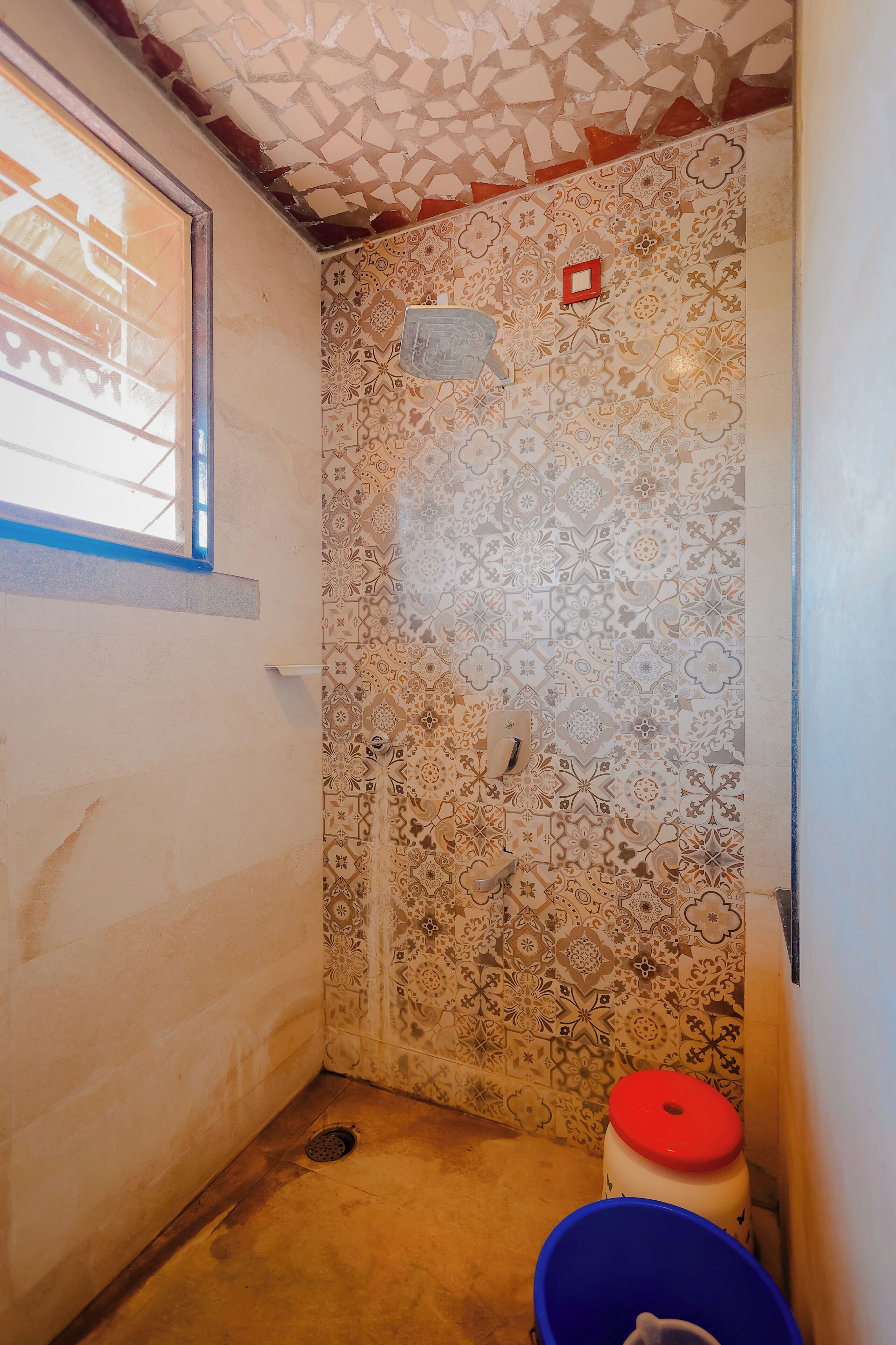 Un baño con baldosas estampadas, una ventana, un inodoro y un cubo azul.