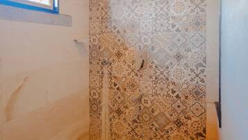 Un baño con baldosas estampadas, una ventana, un inodoro y un cubo azul.
