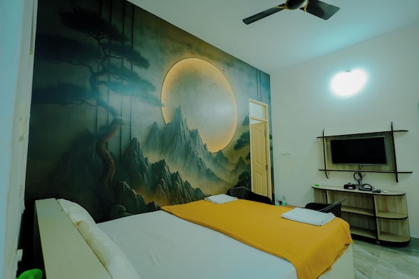 Un dormitorio con cama, escritorio con computadora, televisión y un mural en la pared.