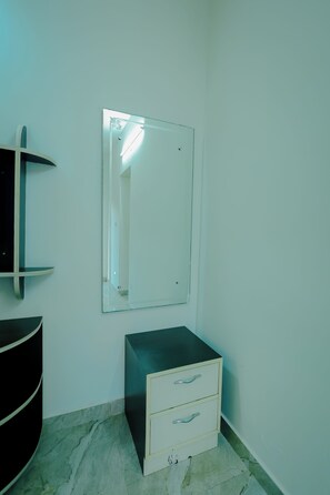 A room with a white wall, a black cabinet, a white bedside table with drawers, and a mirror.