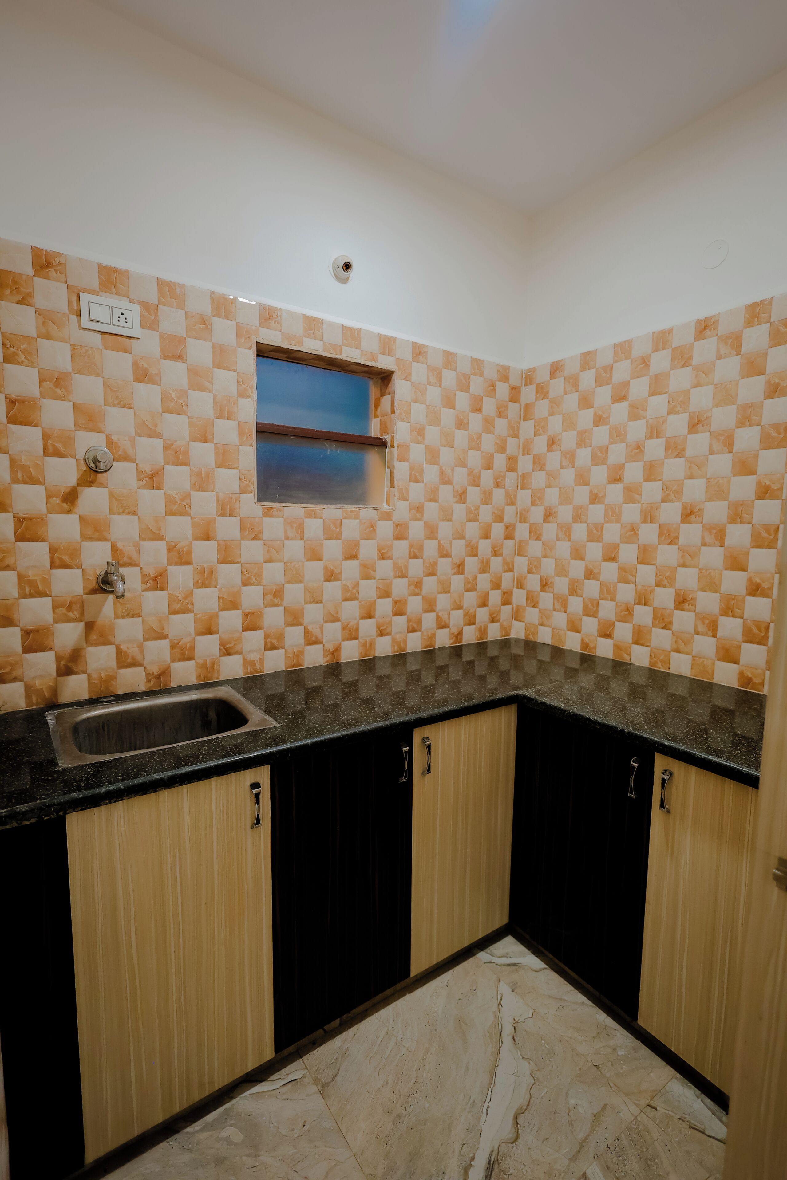 Cozinha com painel de azulejos xadrez, janela, pia e armários de madeira.
