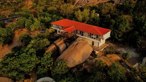 Una casa con techo rojo, rodeada de rocas grandes y árboles.
