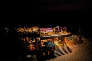 A modern hotel with a glass facade, outdoor seating, and a covered patio area.