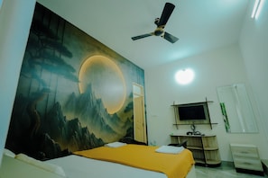 A bedroom with a bed, a ceiling fan, a TV, a desk, and a wall with a painting.