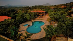 Un resort con una amplia piscina, un pabellón cubierto y montañas al fondo.