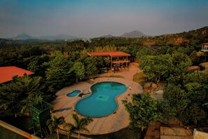 A resort with a large swimming pool, a covered pavilion, and a mountainous backdrop.