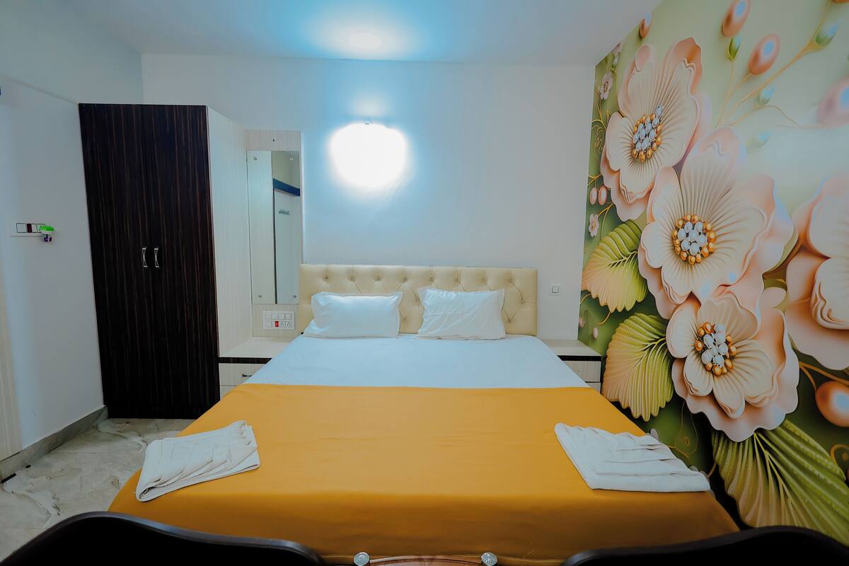 Una habitación de hotel con cama, armario, mesita de noche y pared decorada con un mural floral.