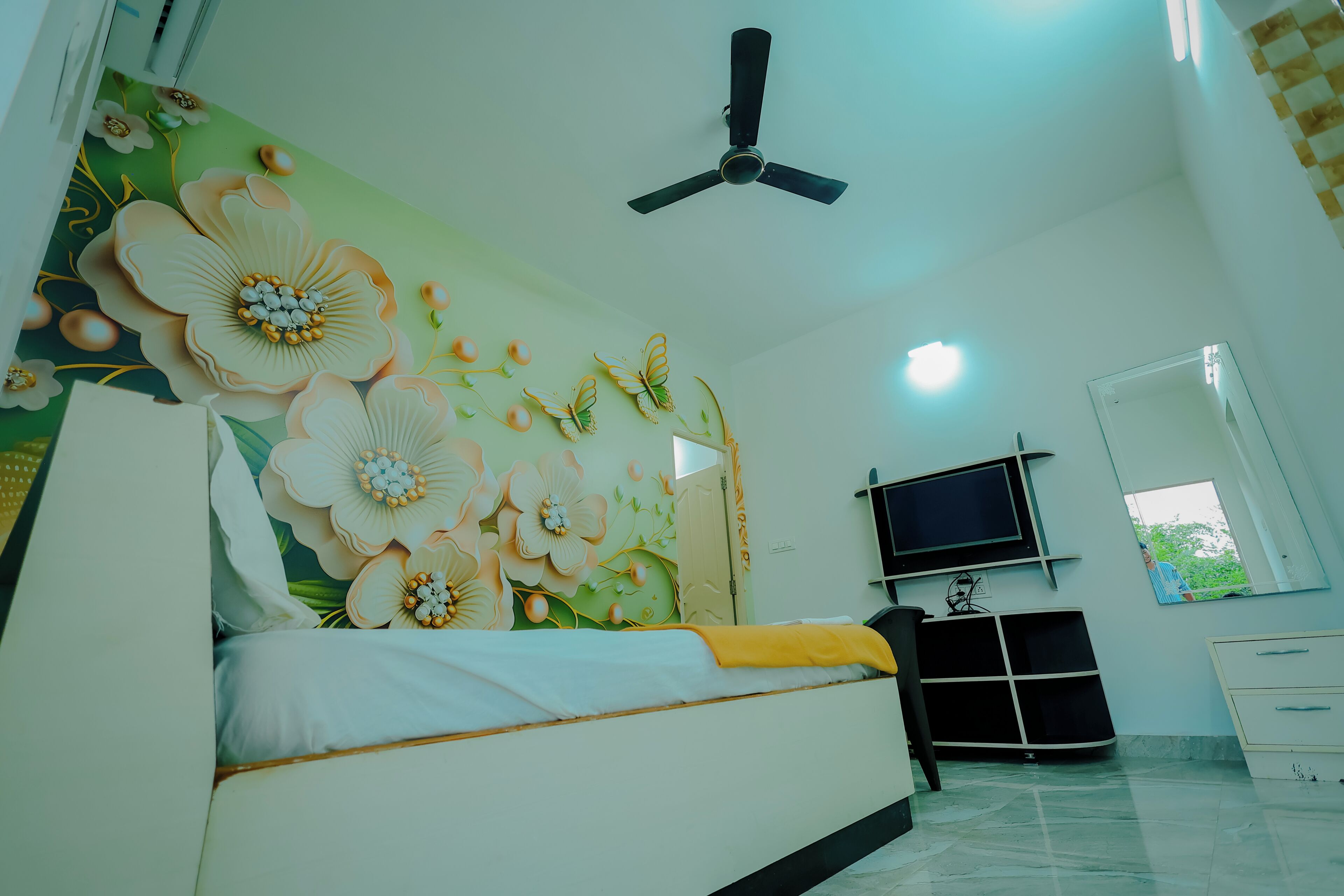 A bedroom with a bed, a ceiling fan, a TV, and a window.