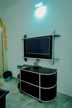 A room with a mounted TV on a wall, a black entertainment unit below it, and a trash bin in the corner.