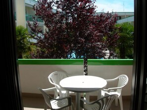 Ein Balkon mit einem weißen Tisch und Stühlen, ein Baum mit roten Blättern und ein Gebäude im Hintergrund.