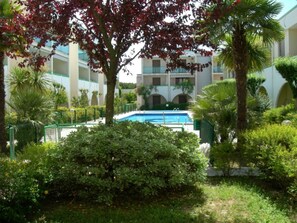 Ein Pool, umgeben von Grünflächen, ein Gebäude mit Balkonen und ein klarer Himmel.