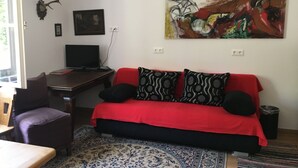 Una habitación con un sofá rojo, cojines estampados, un escritorio con una computadora, un cuadro enmarcado y una decoración de cabeza de ciervo montada en la pared.