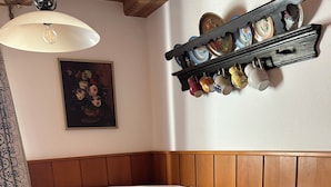 Un comedor con una mesa de madera, sillas blancas, un banco acolchado, una estantería de pared con objetos decorativos y un cuadro.