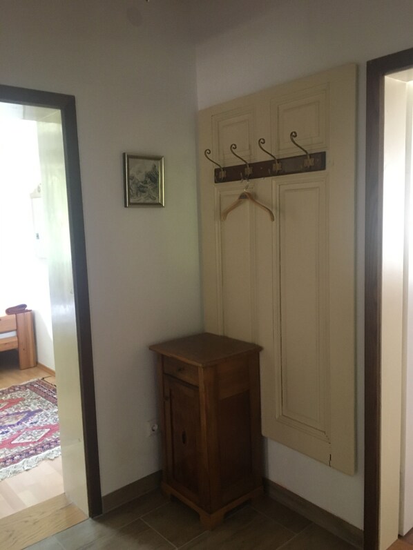 A corner room with a wooden cabinet, a coat rack, and a door with a coat hanging.