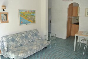 Ein Zimmer mit einer gemusterten Couch, einem Glastisch, einer Karte an der Wand und einer Küchenzeile.