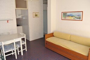 Ein Zimmer mit weißer Ziegelwand, einer Holzbank, einem Tisch mit Stühlen, einer Küchenzeile und einem gerahmten Bild an der Wand.