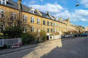 A row of traditional brick buildings with multiple windows, a white picket fence, and bicycles parked along the street. - Terraced house in Komponistkvarteret, Østerbro (København)