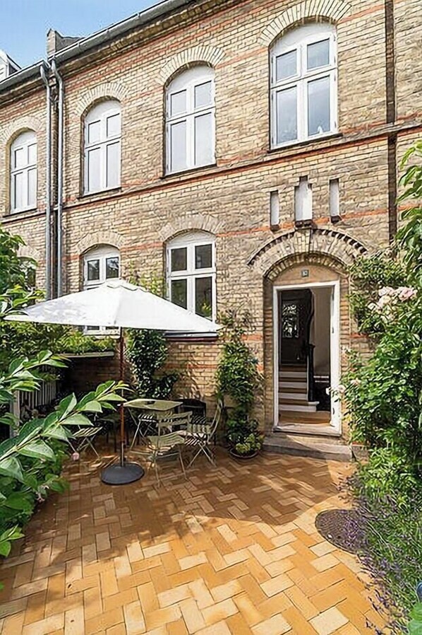 A brick building with a herringbone-patterned patio, outdoor seating, and a door leading to an interior staircase. - Terraced house in Komponistkvarteret, Østerbro (København)