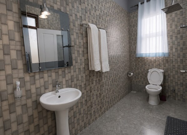 A bathroom with a sink, mirror, towel rack, toilet, shower, and patterned tiles. - ntare gardens mbarara (Mbarara)