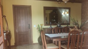 Un comedor con una mesa y sillas de madera, suelo de baldosas, una puerta de madera y un espejo sobre la mesa.