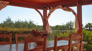 Un área de comedor al aire libre techada, con muebles de madera y una mesa con un centro de mesa floral.