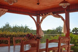 A covered outdoor dining area with wooden furniture and a table with a floral centerpiece. - Monte das Medronheiras House (Boliqueime)