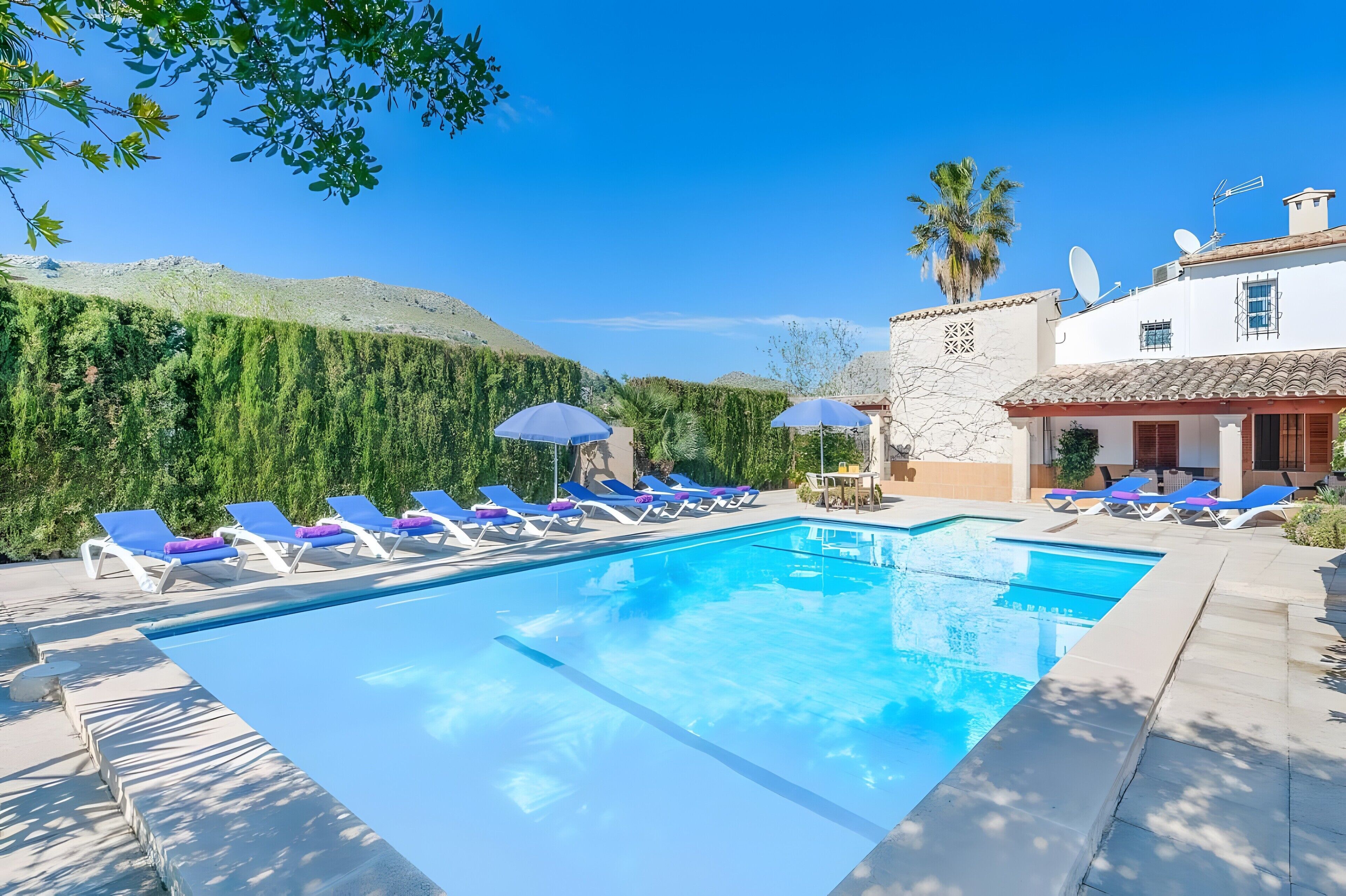 Une piscine avec des chaises longues, un paysage montagneux en arrière-plan et un bâtiment équipé d’antennes paraboliques.
