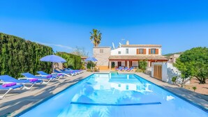 A swimming pool with lounge chairs and umbrellas, a building with a tiled roof, and a palm tree. - Villa 'Palmera' with Private Pool, Wi-Fi and Air Conditioning (El Vilà)