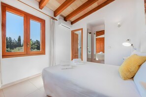 Ein Schlafzimmer mit einem großen Bett, Holzbalken, einem Fenster mit Vorhängen, einer Klimaanlage und einem Spiegel.