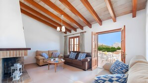A spacious living area with a fireplace, a sofa set, a dining table, and a view through an open door to an outdoor patio. - Villa 'Palmera' with Private Pool, Wi-Fi and Air Conditioning (El Vilà)