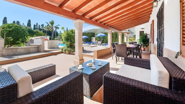 A covered outdoor seating area with wicker furniture and a table, overlooking a pool and greenery. - Villa 'Palmera' with Private Pool, Wi-Fi and Air Conditioning (El Vilà)