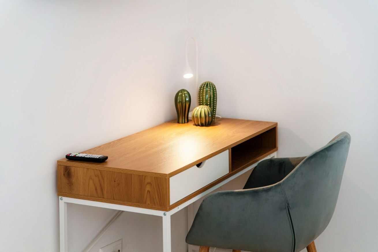 Un bureau en bois avec une télécommande, deux vases décoratifs et une chaise grise.