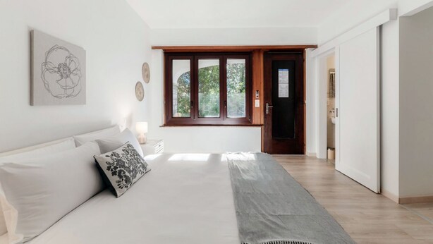 Ein Schlafzimmer mit Bett, Fenster, Tür und einem Gang.
