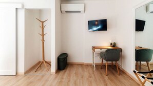Ein modernes Zimmer mit Holzboden, Schreibtisch mit Stuhl, Kleiderhaken, Fernseher und Klimaanlage.