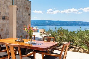 Ein Holztisch mit Stühlen, eine Vase mit Blumen und Blick auf Meer und Hügel.