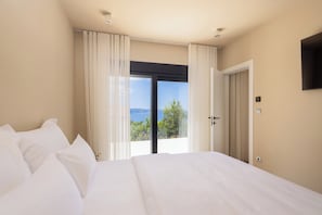 Ein Schlafzimmer mit einem großen Bett, einer Glasschiebetür zu einem Balkon und einem wandmontierten Flachbildfernseher.