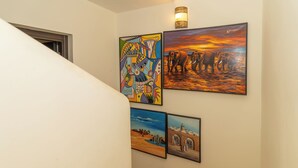 A staircase with a handrail, a wall with four framed artworks, and a light fixture above the artwork.