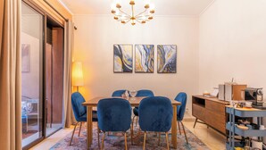 A dining area with a table, chairs, a chandelier, artwork, and a kitchenette.
