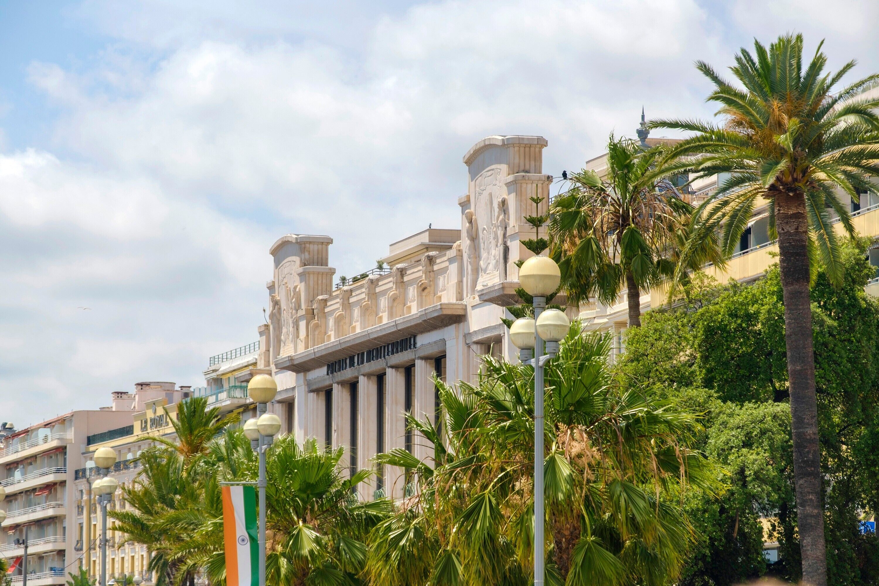 A building with classical architecture, palm trees, and street lamps.