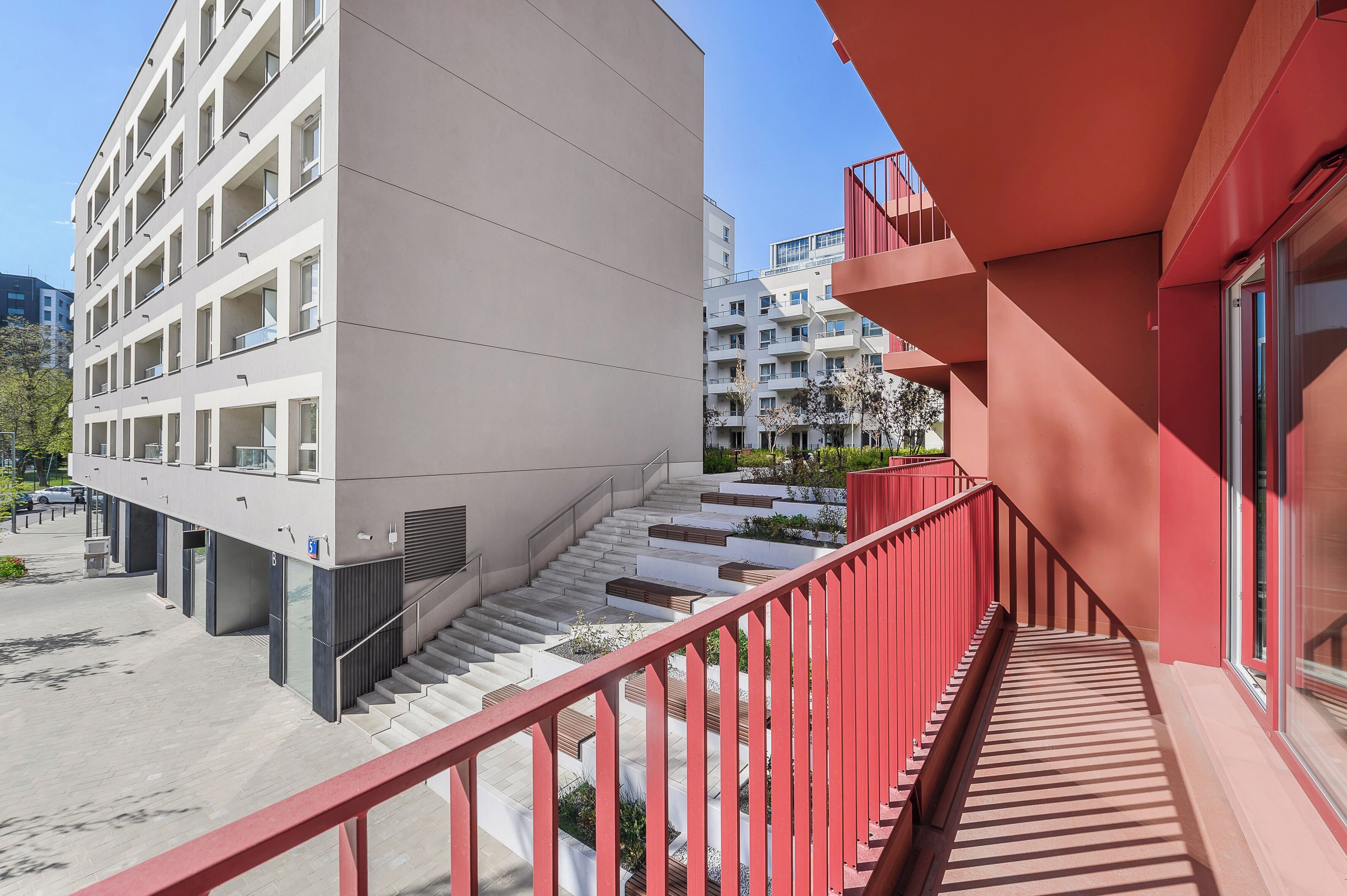 A modern building with a red exterior, a staircase, and a parking area.