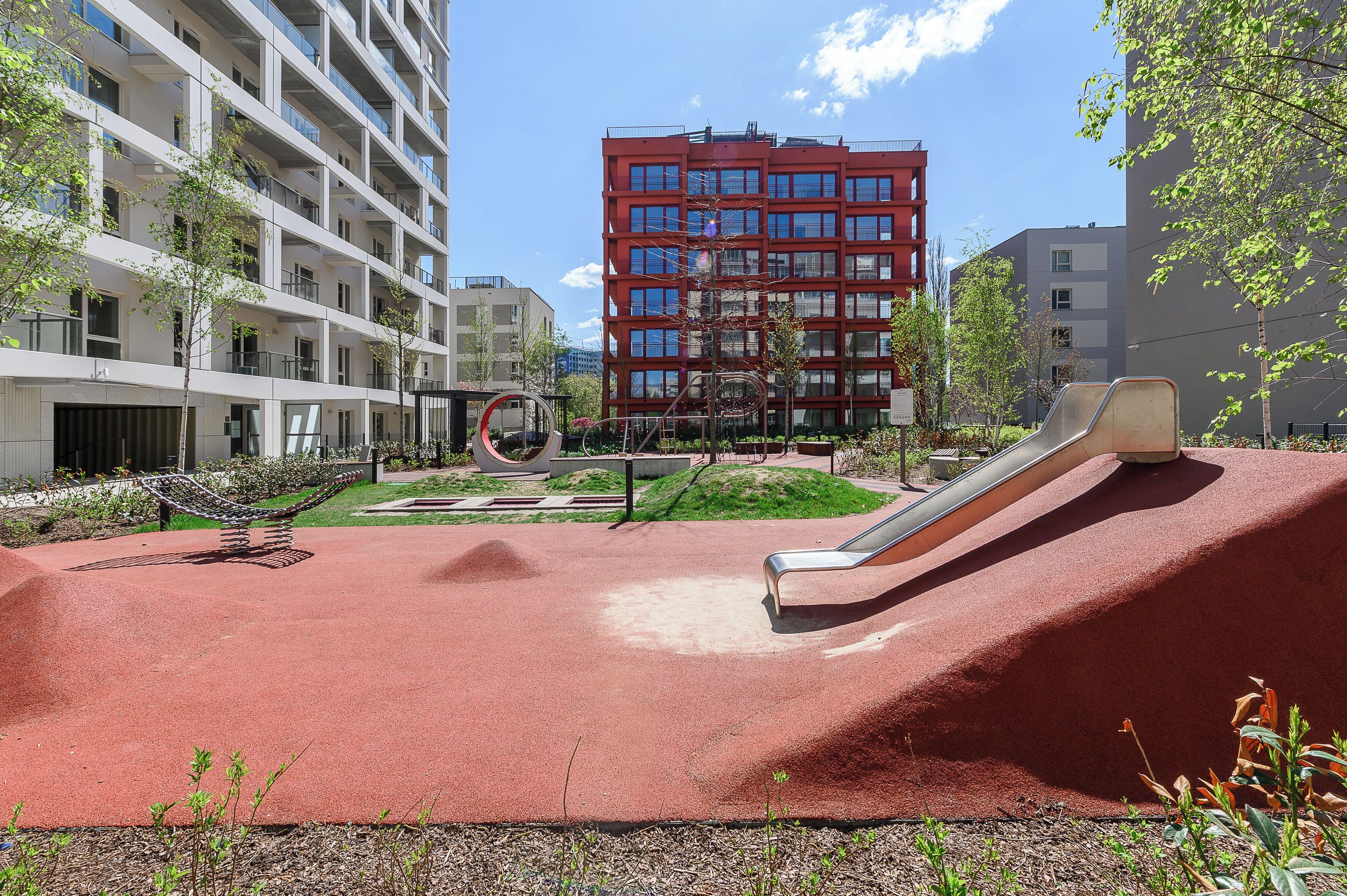 A playground with a slide and climbing structure, surrounded by buildings.