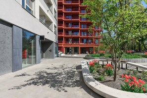 Ein modernes Gebäude mit roter Fassade, ein Innenhof mit roten Blumen und ein Baum.